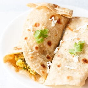 closeup shot of spinach wraps on a white plate topped with some grated cheese and two sprigs of cilantro