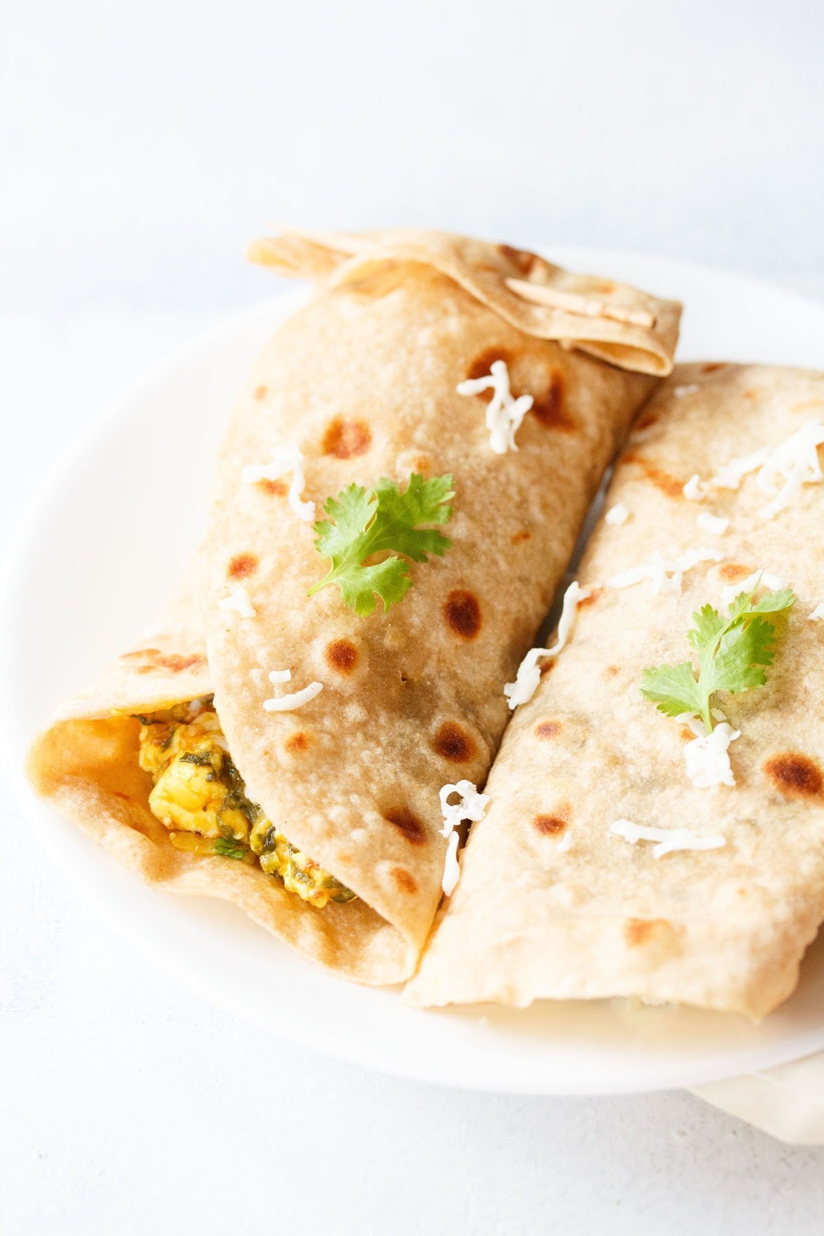 closeup shot of spinach wraps on a white plate topped with some grated cheese and two sprigs of cilantro