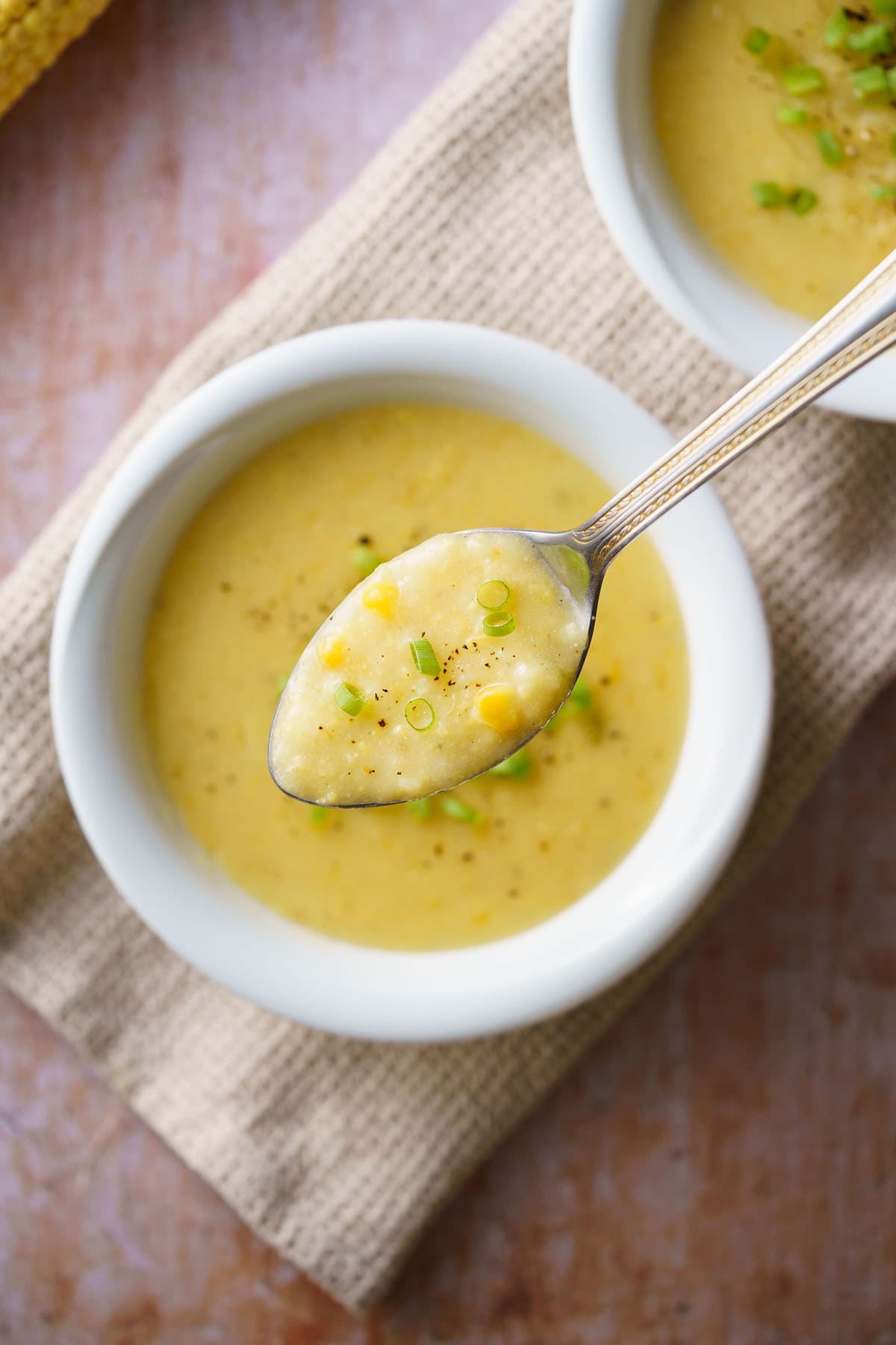 corn soup in a silver spoon on top of white bowl filled with sweet corn soup