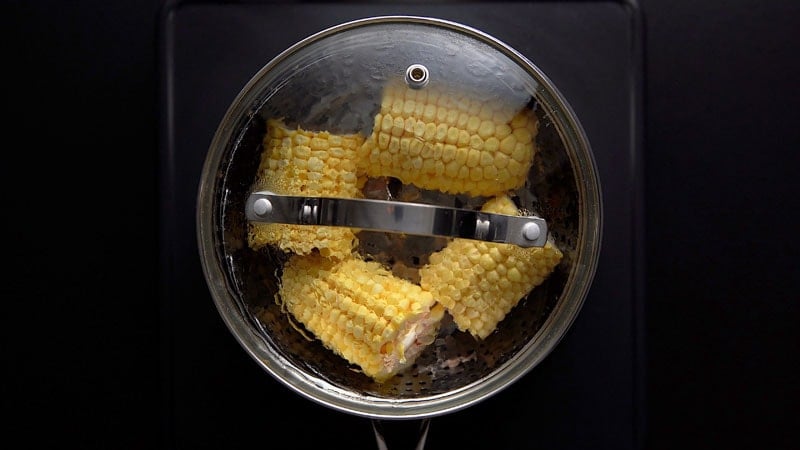 steamer covered with lid and corn cobs being steamed