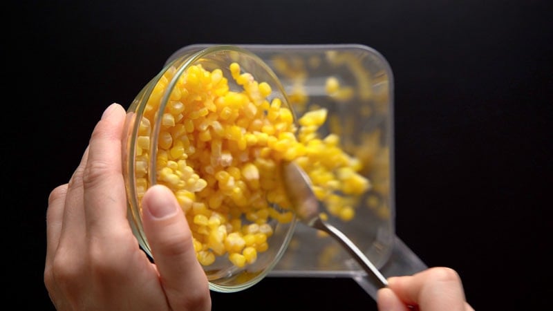 corn kernels being transferred with a spoon in a blender