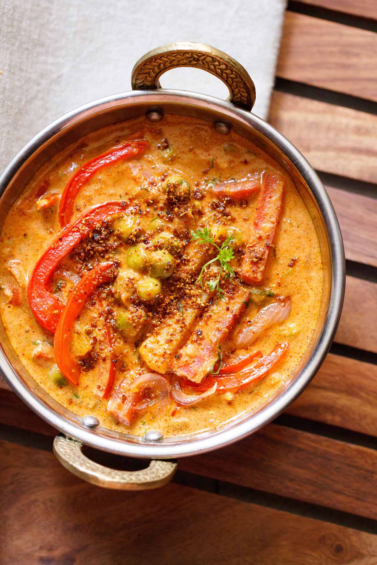 overhead shot of veg kadai in a metal kadai with a white linen on top right side on a wooden board