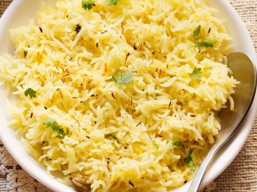 saffron rice or yellow rice with coriander leaves garnish on white plate and spoon on a burlap cloth