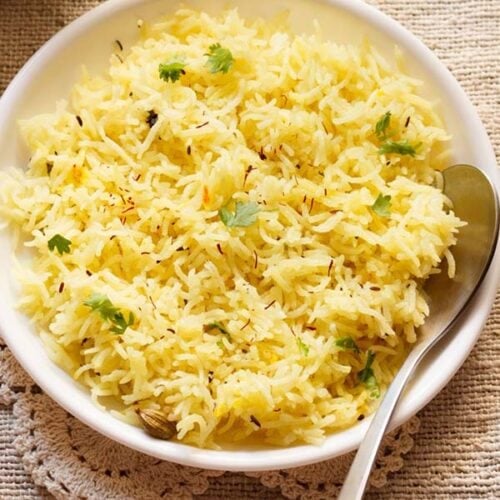 saffron rice or yellow rice with coriander leaves garnish on white plate and spoon on a burlap cloth
