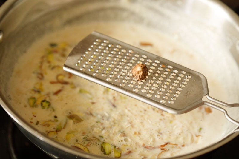 a small piece of nutmeg being grated using a fine grater on top of pan