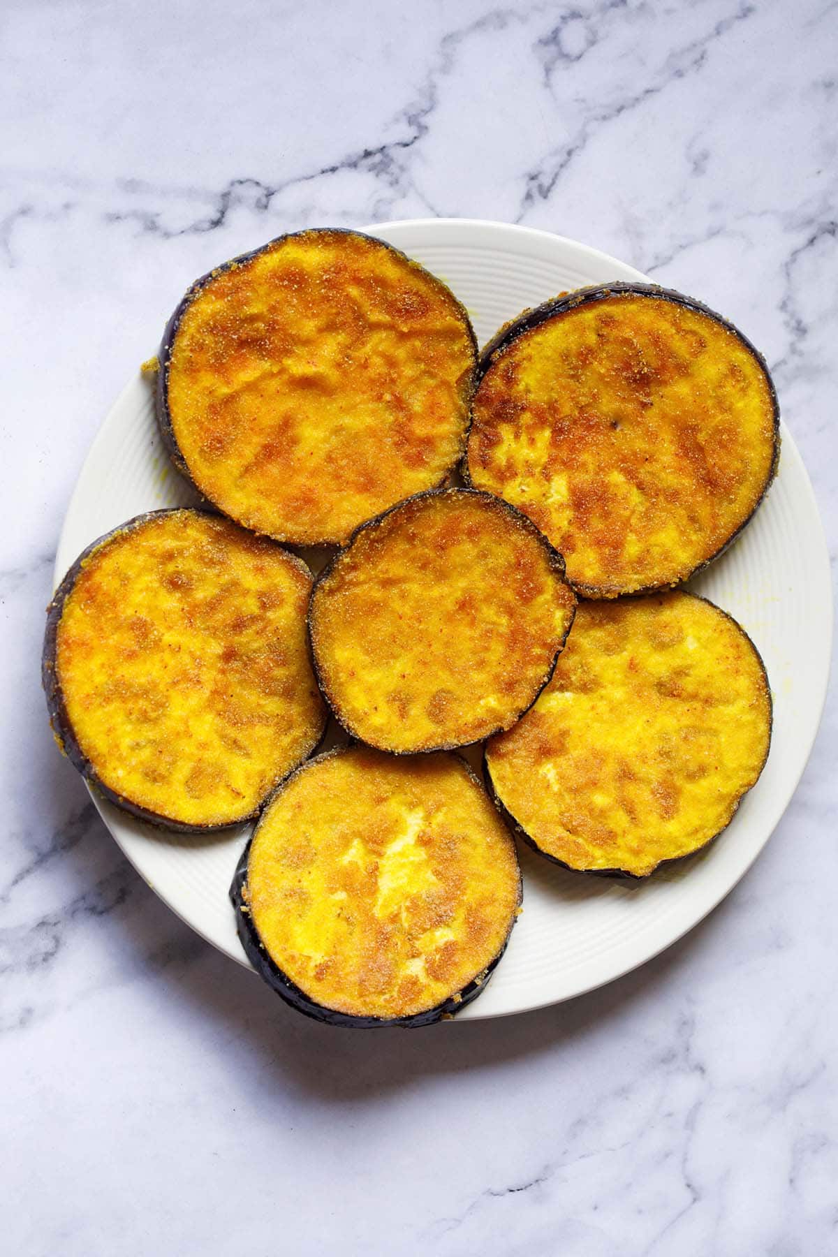 overhead shot of begun bhaja or baingan bhaja slices in a cream colored plate