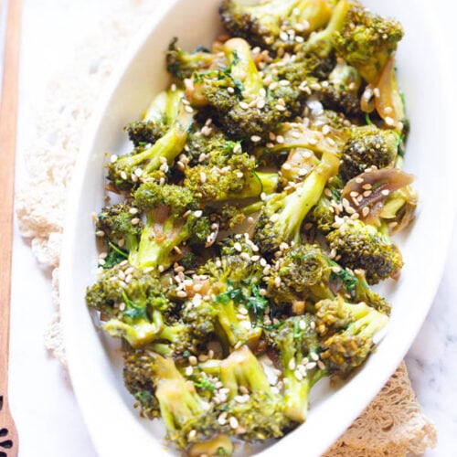 broccoli stir fry in a white oval plate with wooden chopsticks by the side