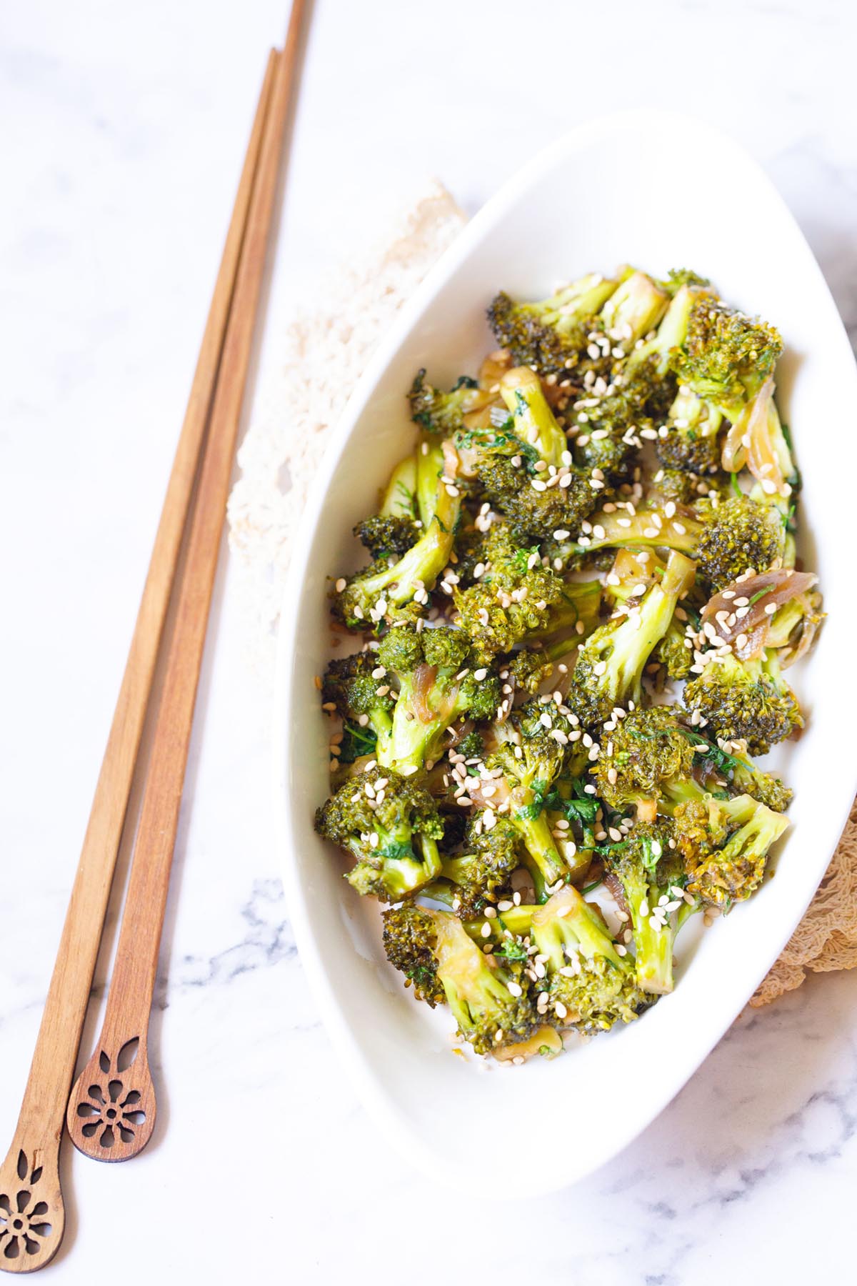 overhead shot of broccoli stir fry in a white oval plate with wooden chopsticks by the side