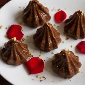 chocolate mode on a white plate garnished crumbled pistachio and decorated with red rose petals