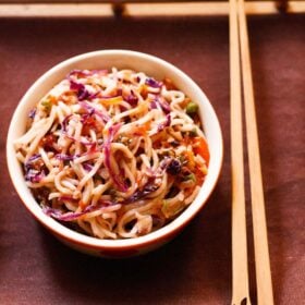 overhead shot of chowmein in a bowl with bamboo chopsticks by the side on a dark brown cotton napkin