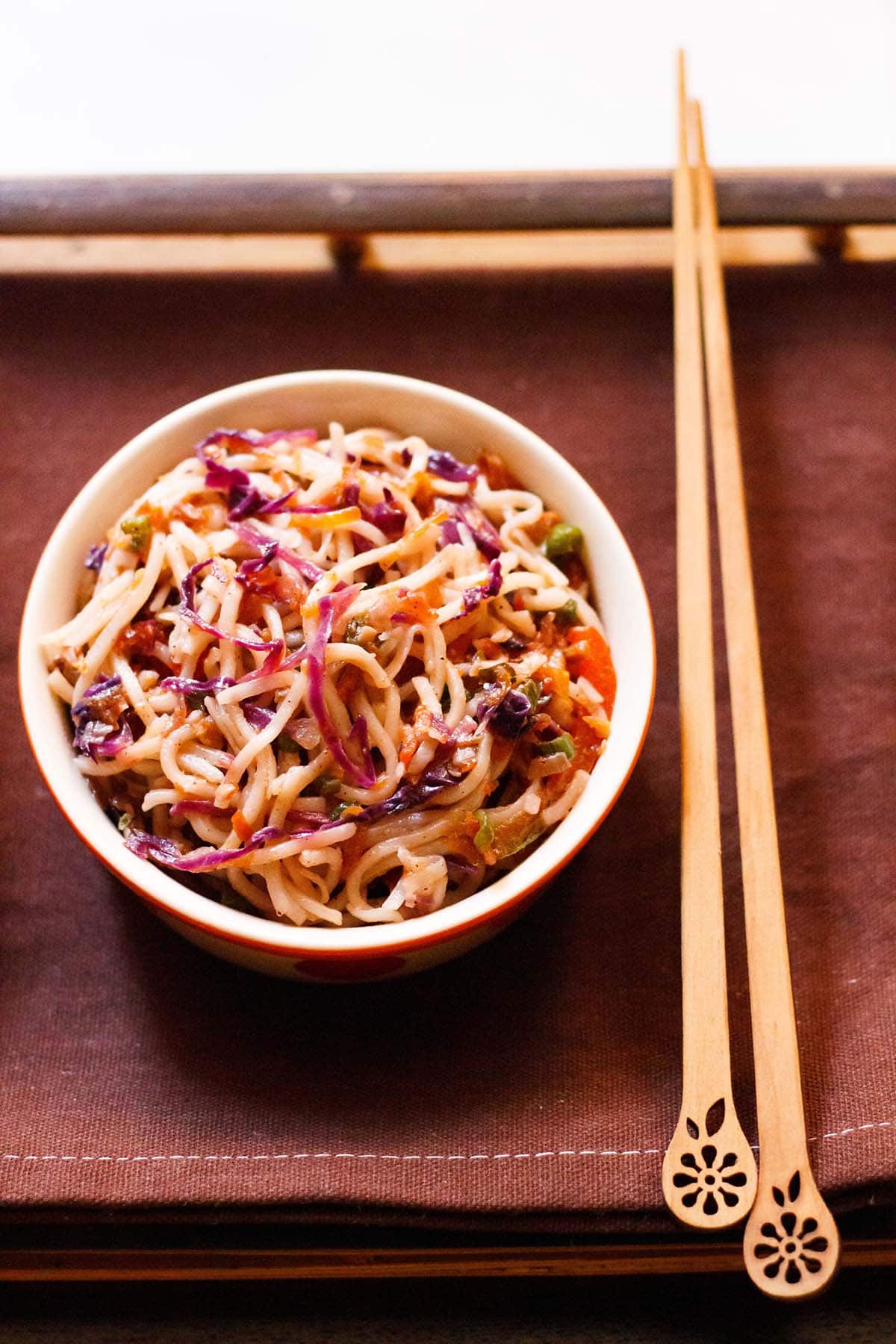 overhead shot of chowmein in a bowl with bamboo chopsticks by the side on a dark brown cotton napkin