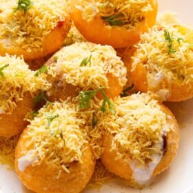 closeup shot of dahi sev batata puri sprinkled with sev and coriander leaves on a white plate.