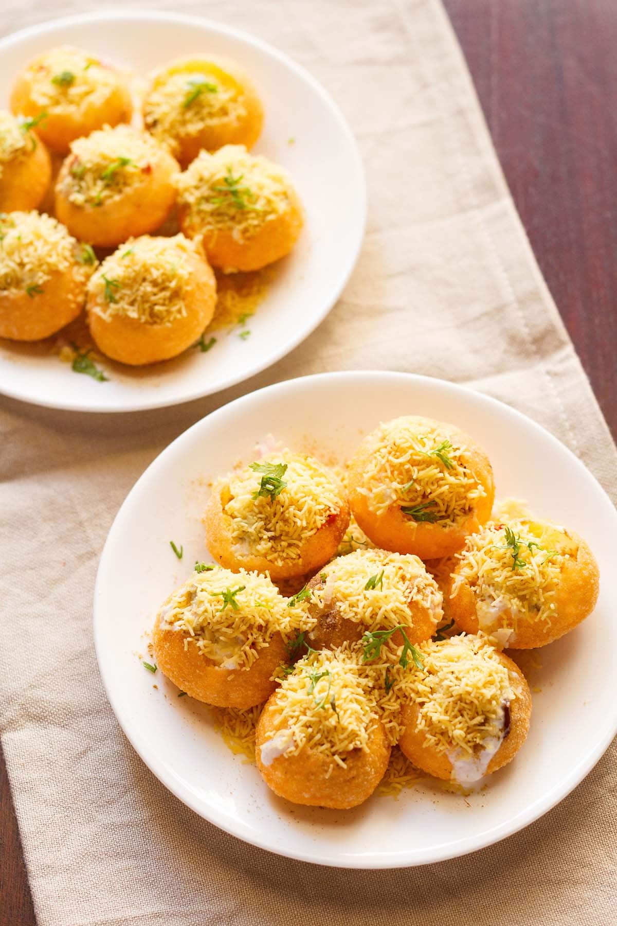 overhead shot of dahi puri in two plates on a beige cotton napkin