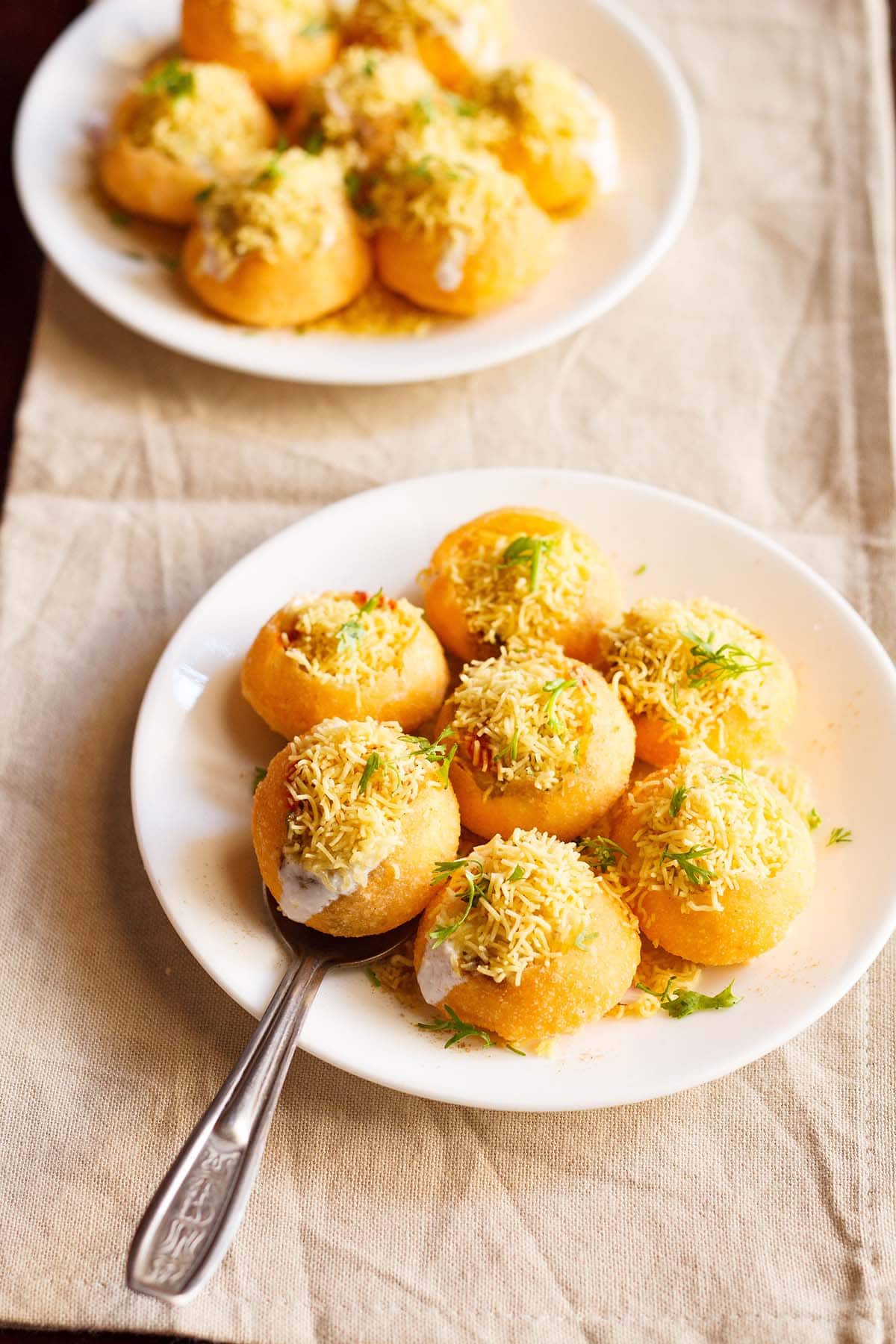 one dahi puri taken in a spoon on a white plate