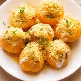 closeup shot of dahi sev batata puri sprinkled with sev and coriander leaves on a white plate.