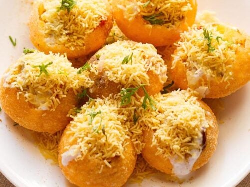 closeup shot of dahi sev batata puri sprinkled with sev and coriander leaves on a white plate.