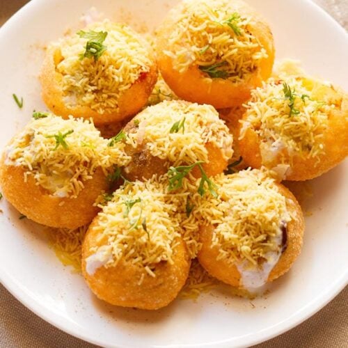 closeup shot of dahi sev batata puri sprinkled with sev and coriander leaves on a white plate.