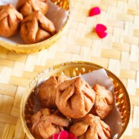 fried modak in a round bamboo bowl with a dark pink flower placed on a bamboo mat