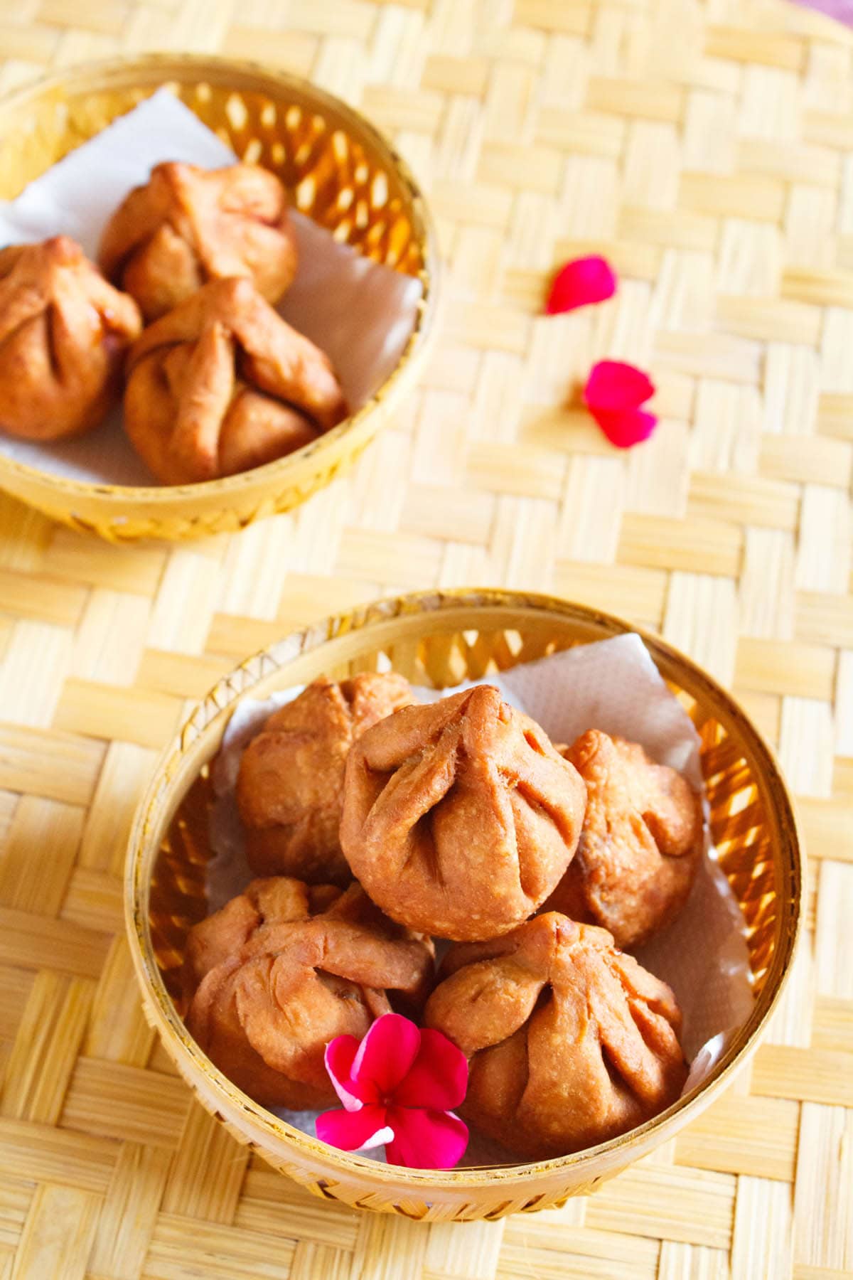 fried modak in a round bamboo bowl with a dark pink flower placed on a bamboo mat