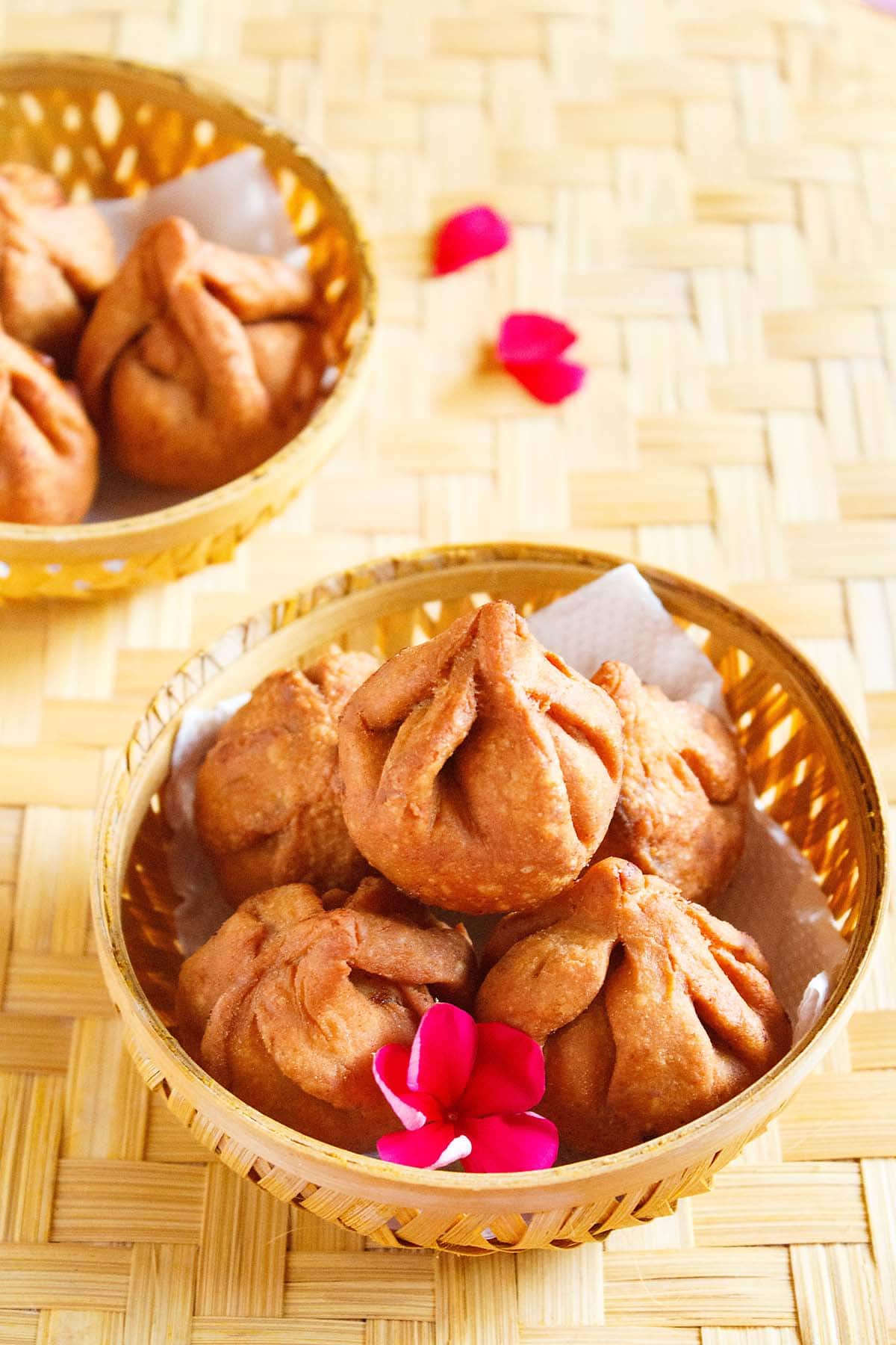 fried modak in a round bamboo bowl with a dark pink flower placed on a bamboo mat