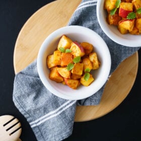 overhead shot of fruit chaat in white bowls placed on a cotton gray napkin on a round bamboo board