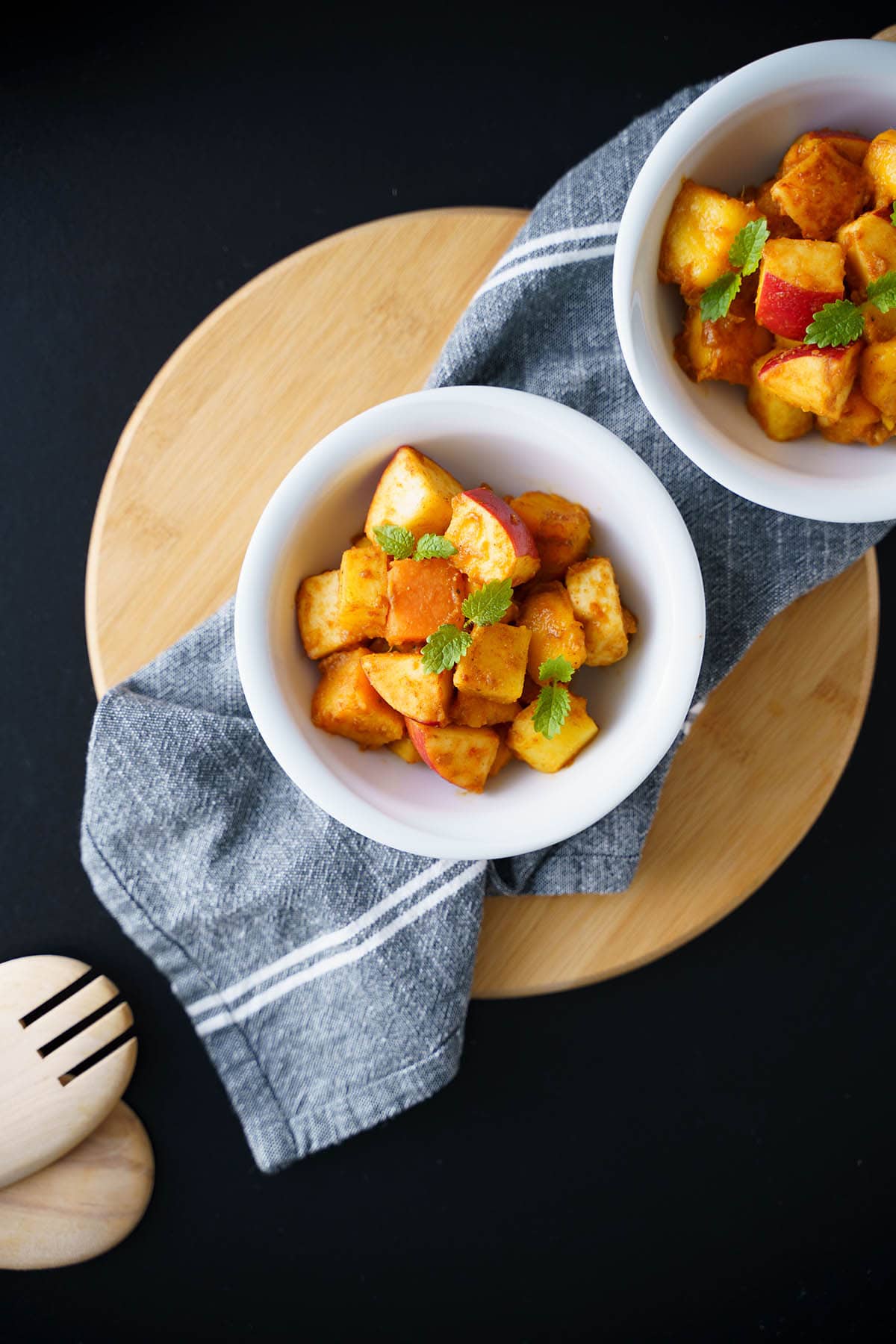 overhead shot of fruit chaat in white bowls placed on a cotton gray napkin on a round bamboo board