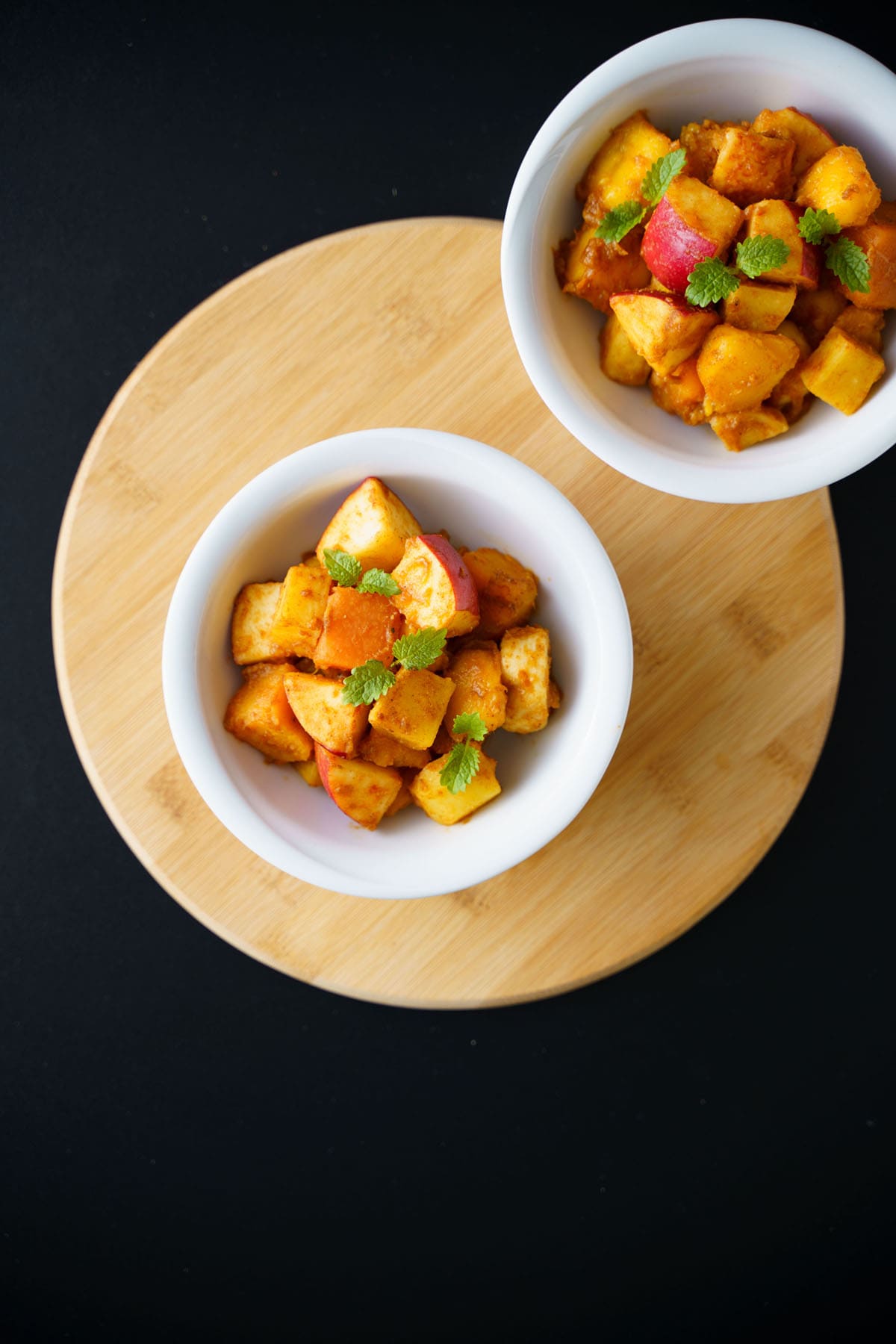 overhead shot of fruit chaat in white bowls on a round bamboo board