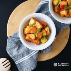 overhead shot of fruit chaat in white bowls placed on a cotton gray napkin on a round bamboo board with text layovers.