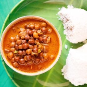 overhead shot of kadala curry in a green bowl on a green plate with two puttu by the side