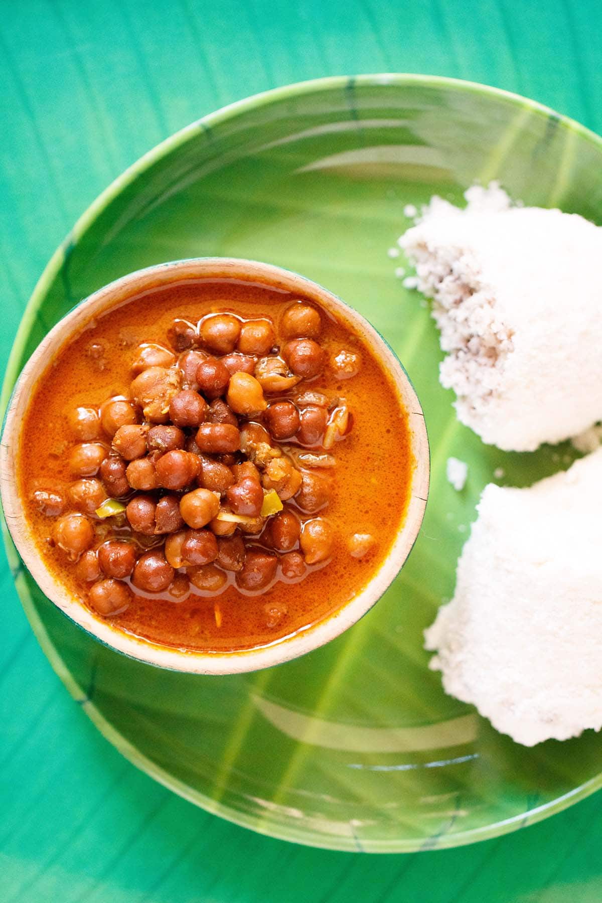 overhead shot of kadala curry in a green bowl on a green plate with two puttu by the side