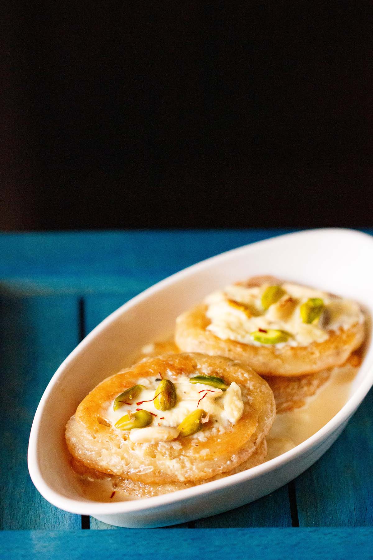 malpua with rabdi served in a oval plate on a dark blue tray