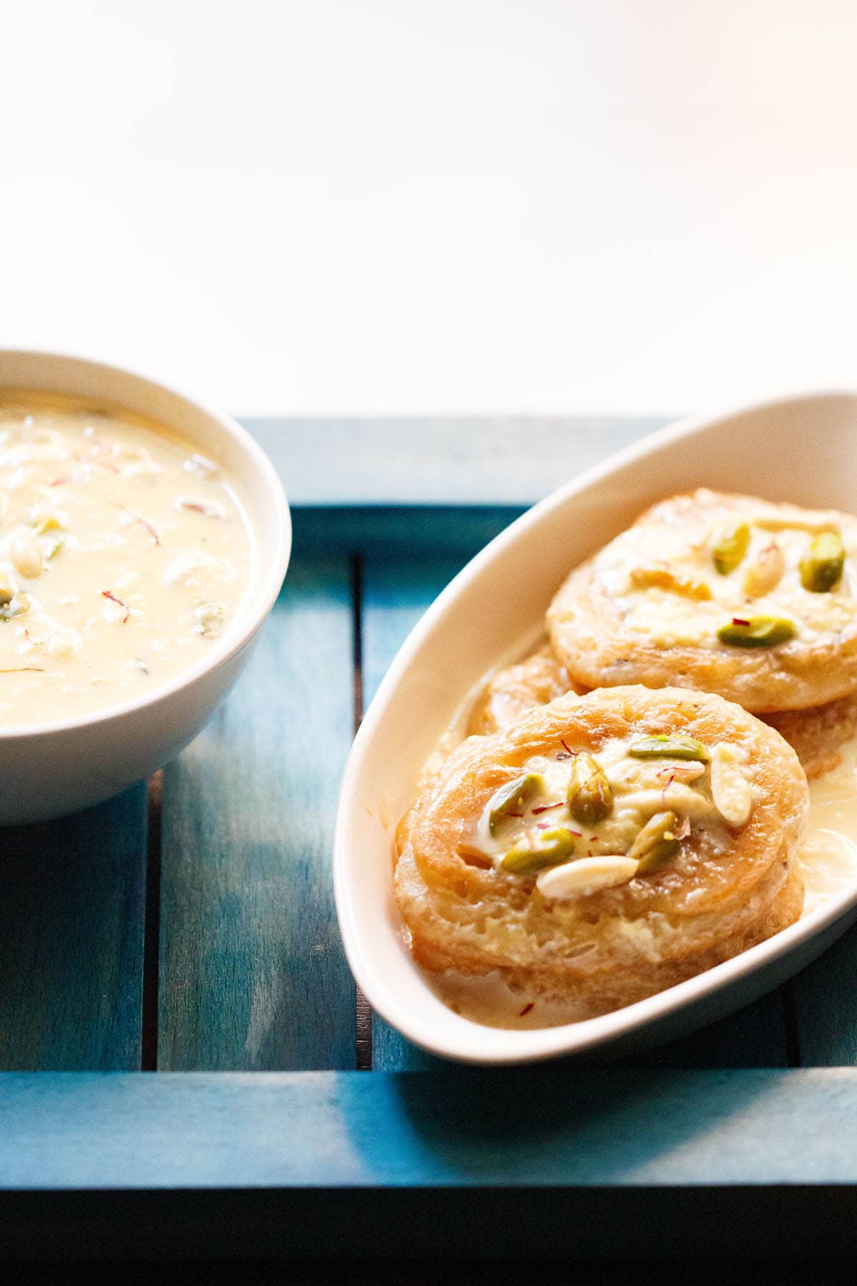 malpua with rabdi served in a oval plate on a dark blue tray with a side white bowl filled with rabdi