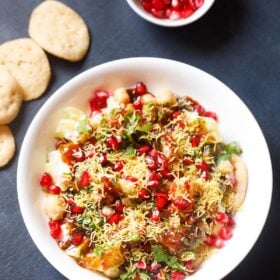 overhead shot of papdi chaat in a white shallow bowl with a side of papdi and pomegranate arils in a small white bowl