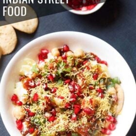 overhead shot of papdi chaat served in a white bowl with a side of papdi and pomegranate arils with text layovers.