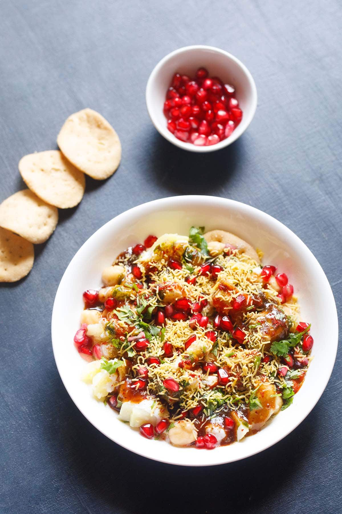 papri chaat in a shallow white bowl with a layer of papdi and pomegranate arils in white bowl