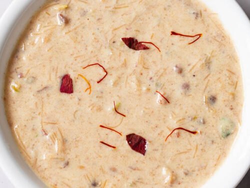 sheer khurma garnished with some saffron strands and rose petals in a white bowl