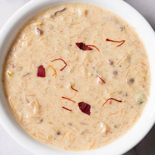 sheer khurma garnished with some saffron strands and rose petals in a white bowl
