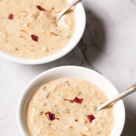 sheer khurma in two white bowls with spoons inside on a marble table