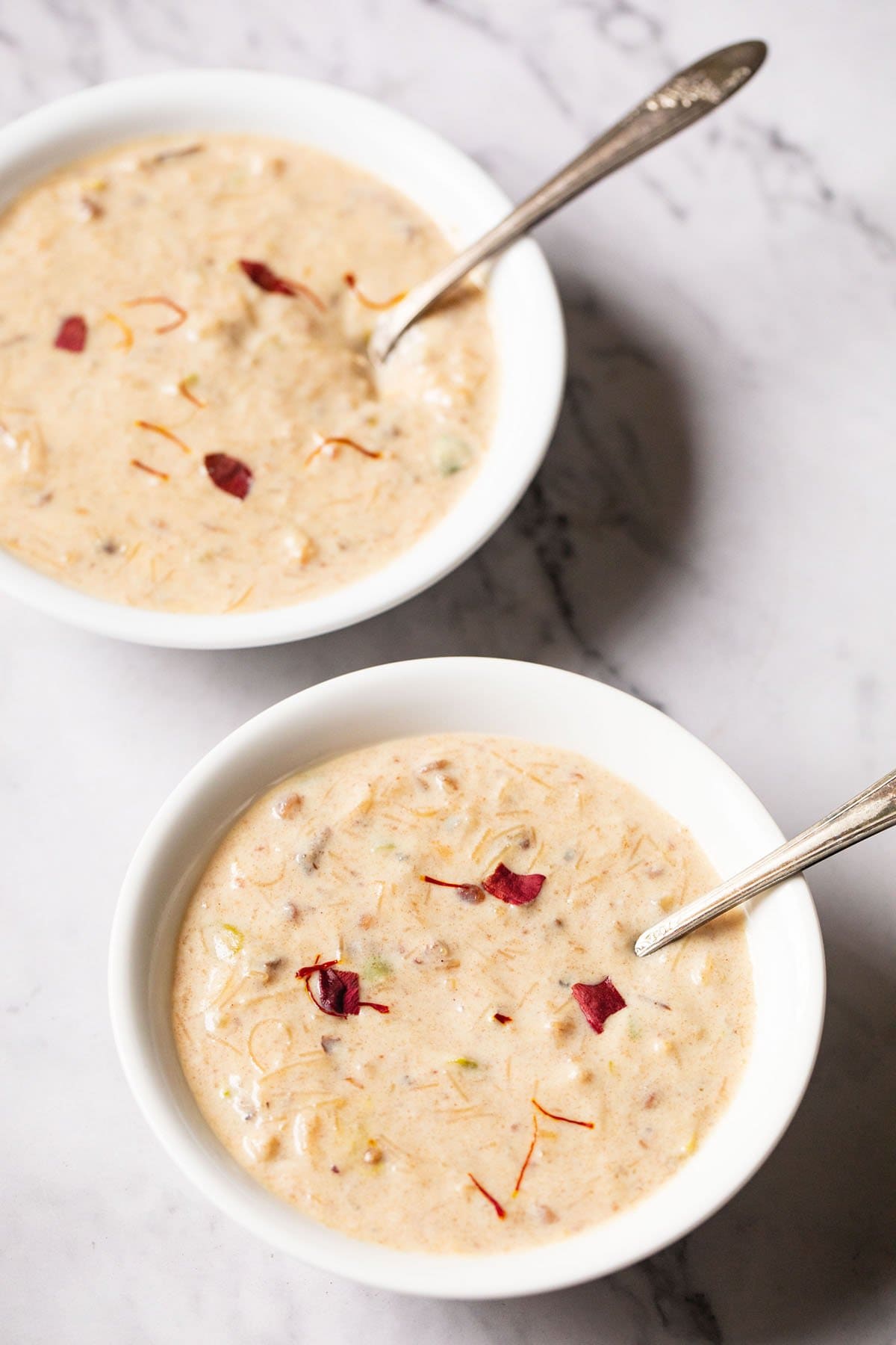 sheer khurma in two white bowls with spoons inside on a marble table