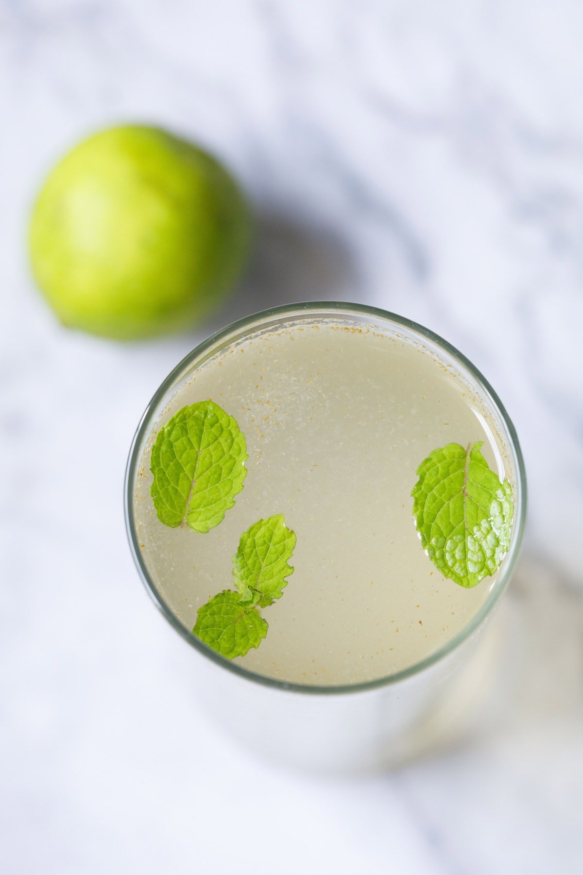 overhead shot of closeup shot of shikanji in a glass with mint leaves with a lemon placed near top left of the glass