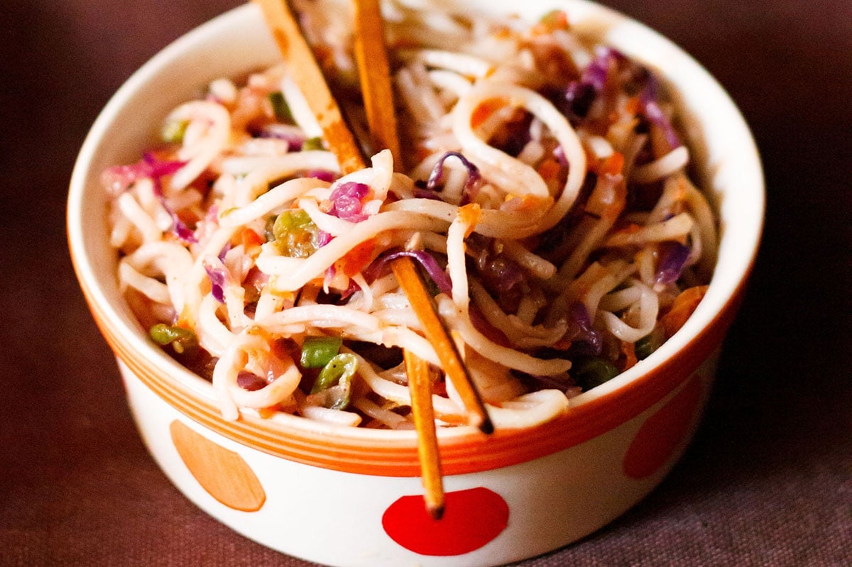 veg chowmein in an orange and white bowl with a pair of wooden chopsticks