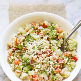 vegetable salad topped with crumbled feta and parsley with a spoon in a white bowl