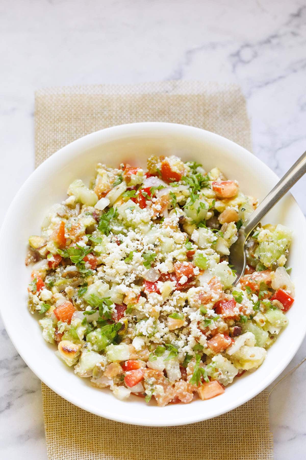 vegetable salad topped with crumbled feta and parsley with a spoon in a white bowl