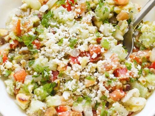 vegetable salad topped with crumbled feta and parsley with a spoon in a white bowl