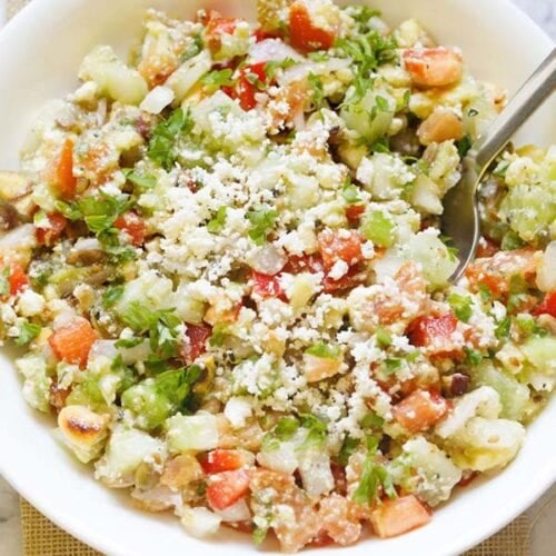 vegetable salad topped with crumbled feta and parsley with a spoon in a white bowl