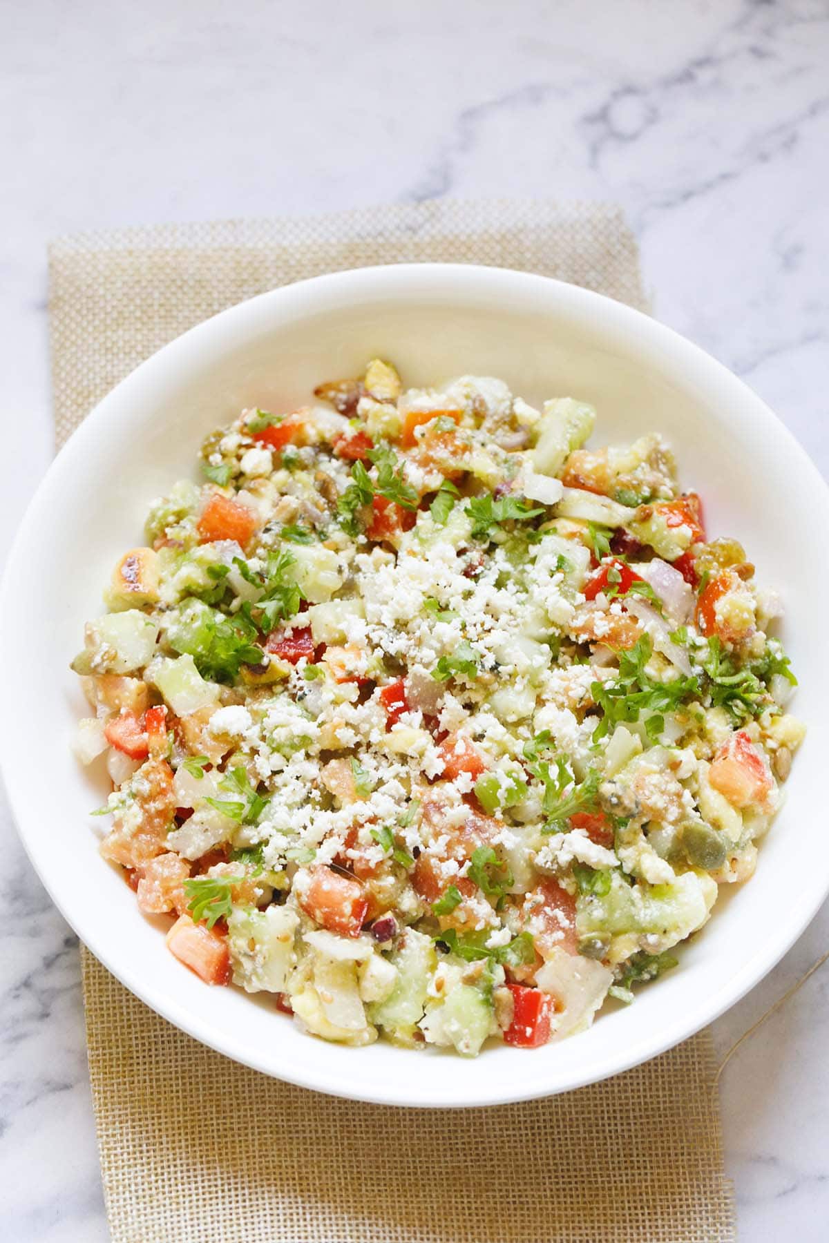 overhead shot of vegetable salad topped with crumbled feta and parsley in a white bowl