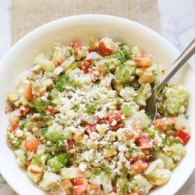 top shot of vegetable salad topped with crumbled feta and parsley with a spoon in a white bowl with text layovers