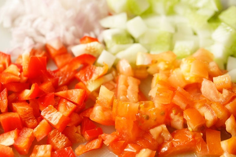 evenly diced onions, cucumbers, tomatoes and bell pepper on a cutting board