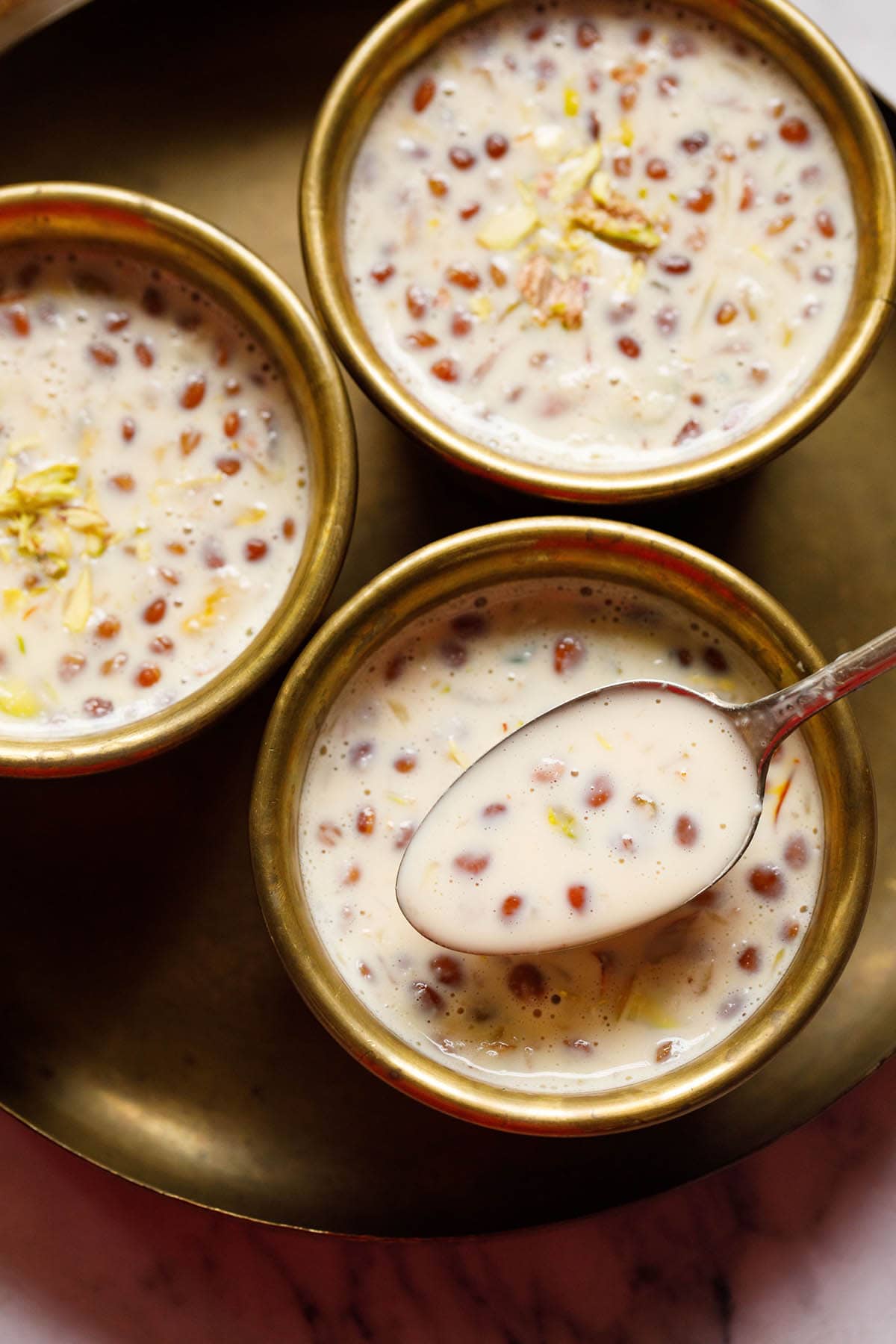 three bowls filled with basundi with a brass spoon containing basundi on top of one bowl