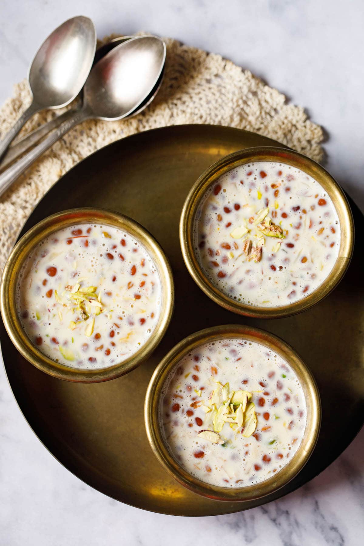 three brass bowls filled with basundi on a brass plate